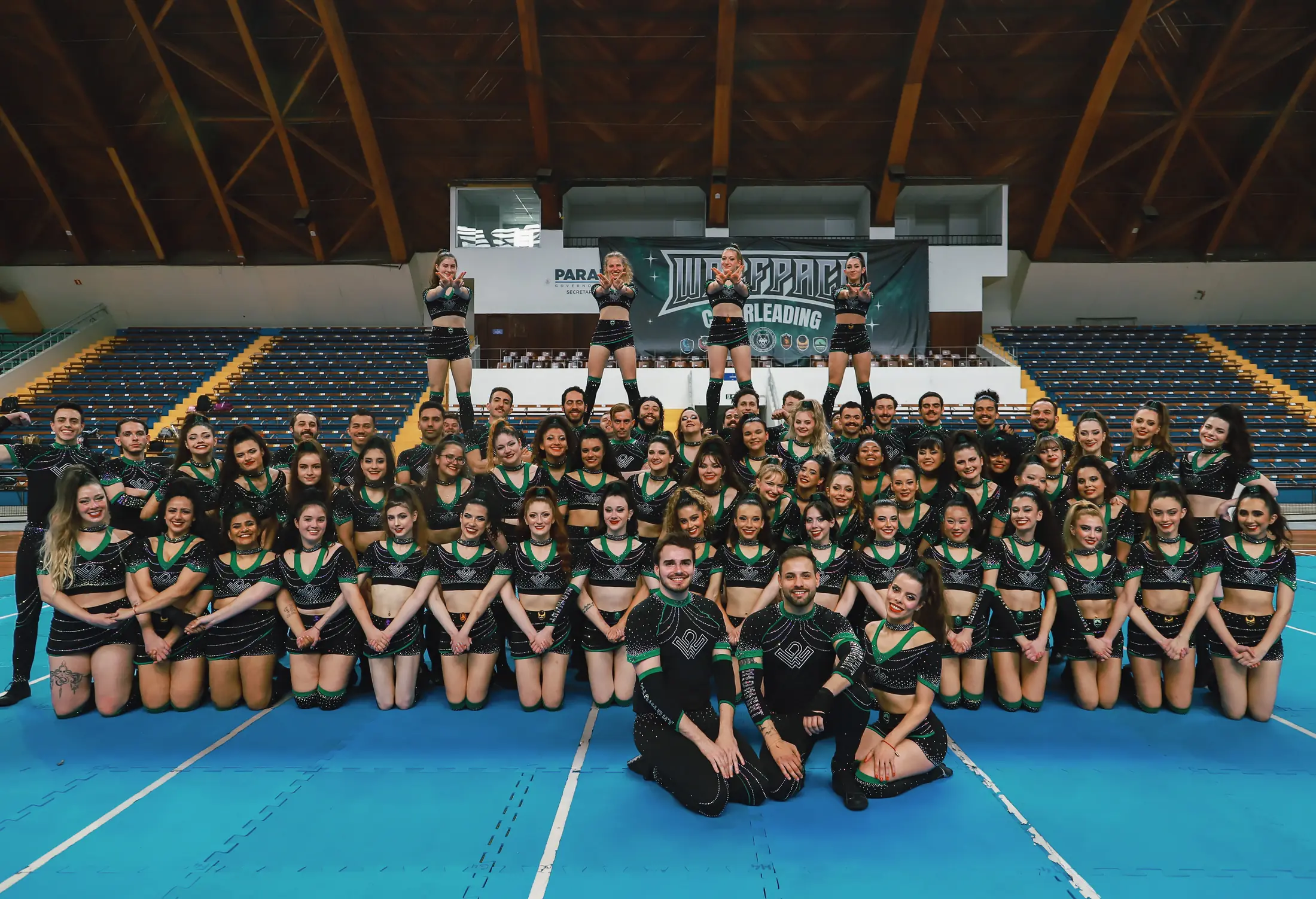 Todas as equipes da Wolfpack reunidas no tablado do Showcase 2025, diante do banner Wolfpack Cheerleading